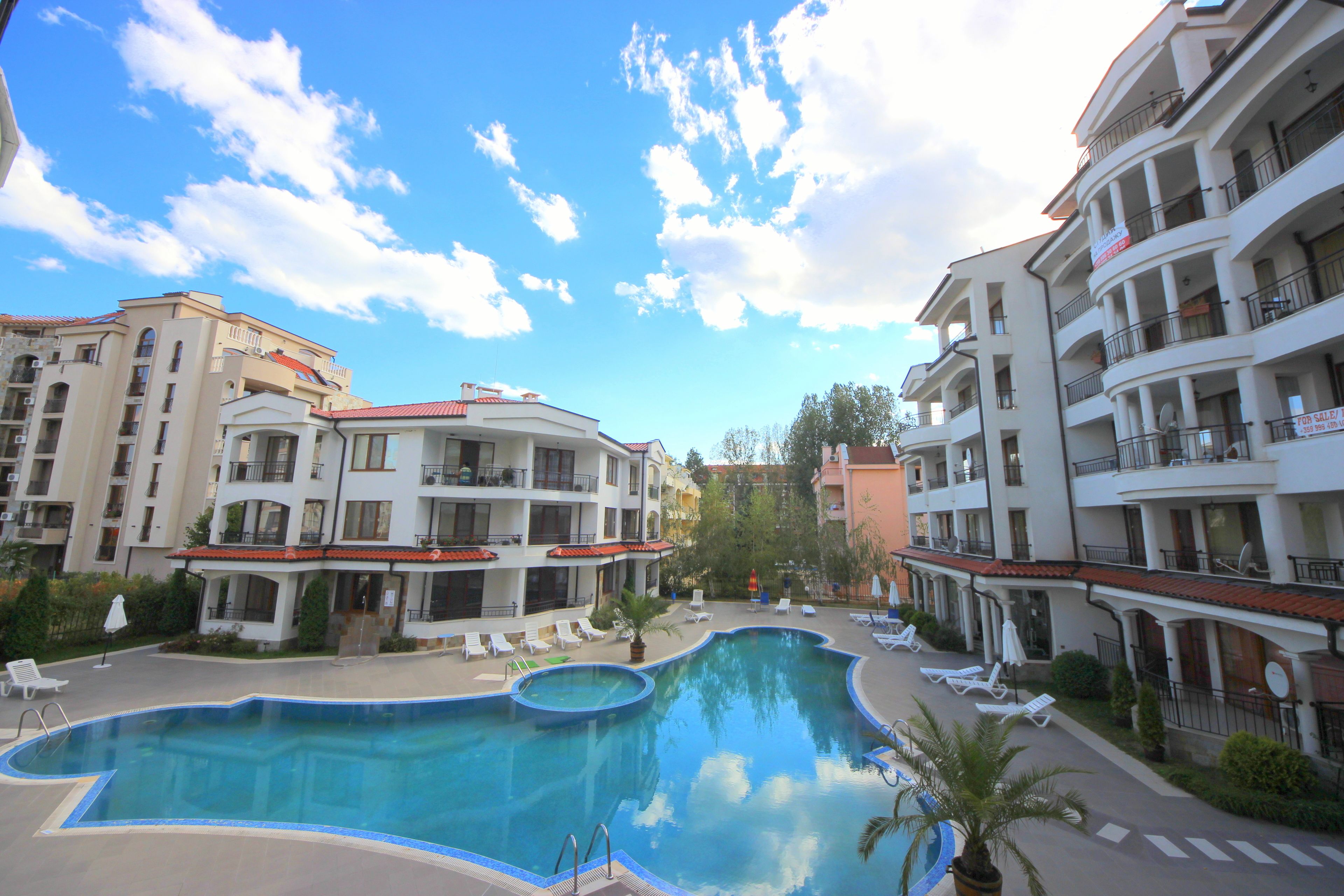 A swimming pool surrounded by multi-story buildings with balconies and a clear sky.