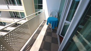 Ein Balkon mit kariertem Boden, einem weißen Stuhl und einem Tisch mit blauer Tischdecke.