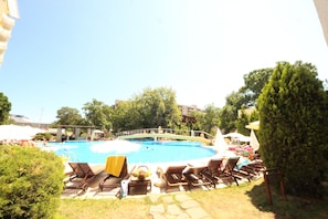 A swimming pool with lounge chairs and umbrellas, surrounded by trees and buildings.