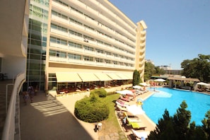 A hotel with a swimming pool, outdoor seating, and a large building with multiple floors.