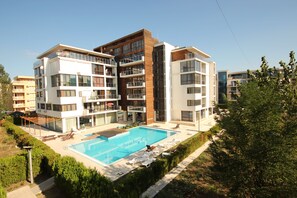 A modern multi-story building with a swimming pool, outdoor seating, and a well-maintained garden area. - Menada Eden Apartments (Sunny Beach)
