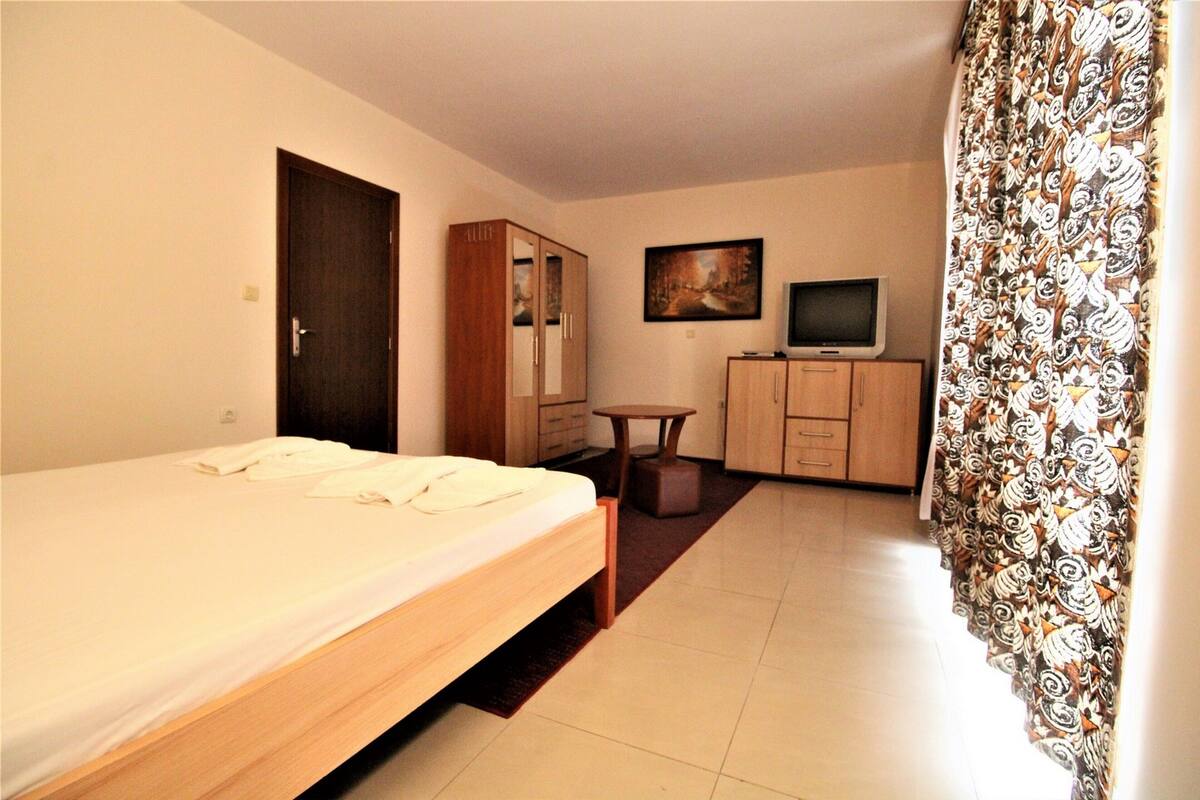 A hotel room with a bed, wardrobe, desk, television, and patterned curtains.