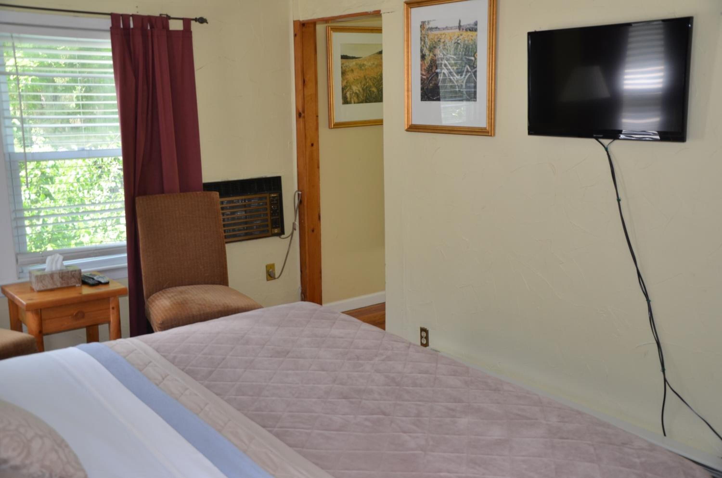 A hotel room with a bed, a chair, a TV, and a window with curtains.