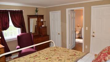 A bedroom with a bed, a chair, a dresser, and a mirror. There are two doors, one leading to a bathroom.