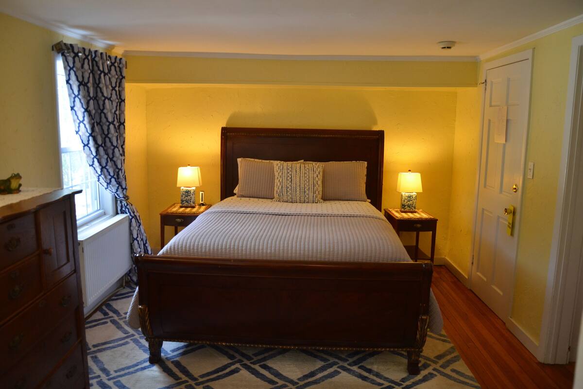 A bedroom with a wooden bed, two bedside lamps, a dresser, and a patterned rug.