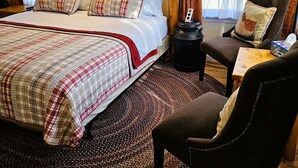 Una habitación de hotel con una cama grande, dos lámparas de noche, una silla, una mesita y una alfombra.