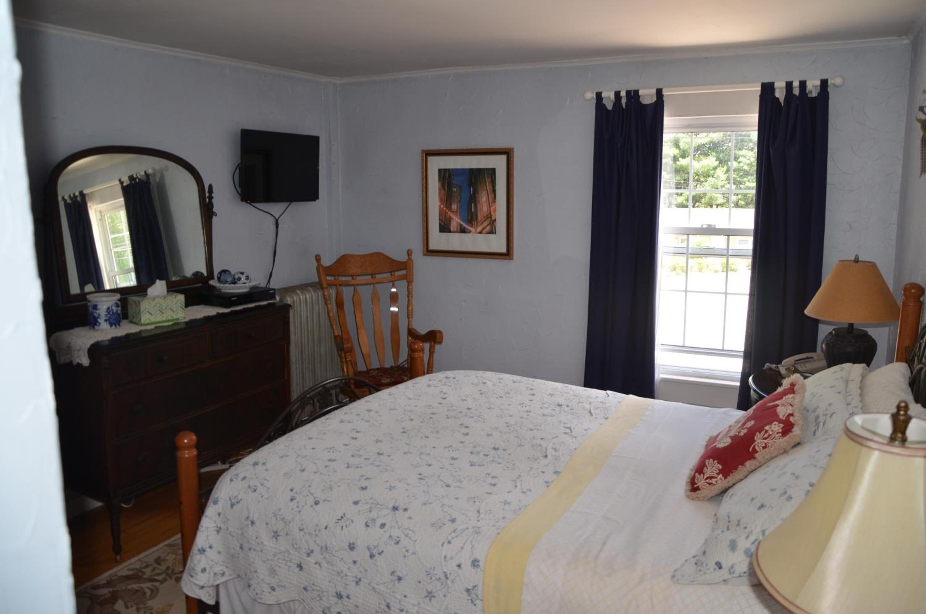 Un dormitorio con cama, cómoda, silla y ventana con cortinas.