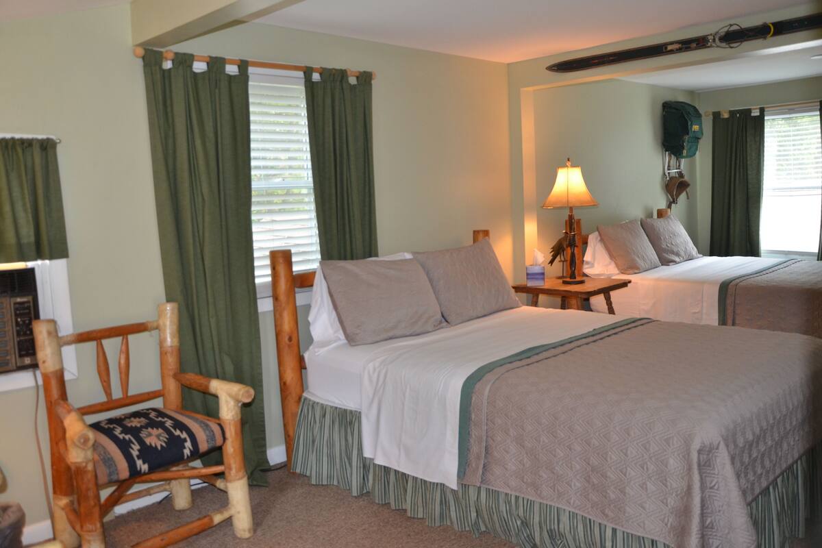 A room with two beds, a wooden chair, a lamp, and a ski rack.