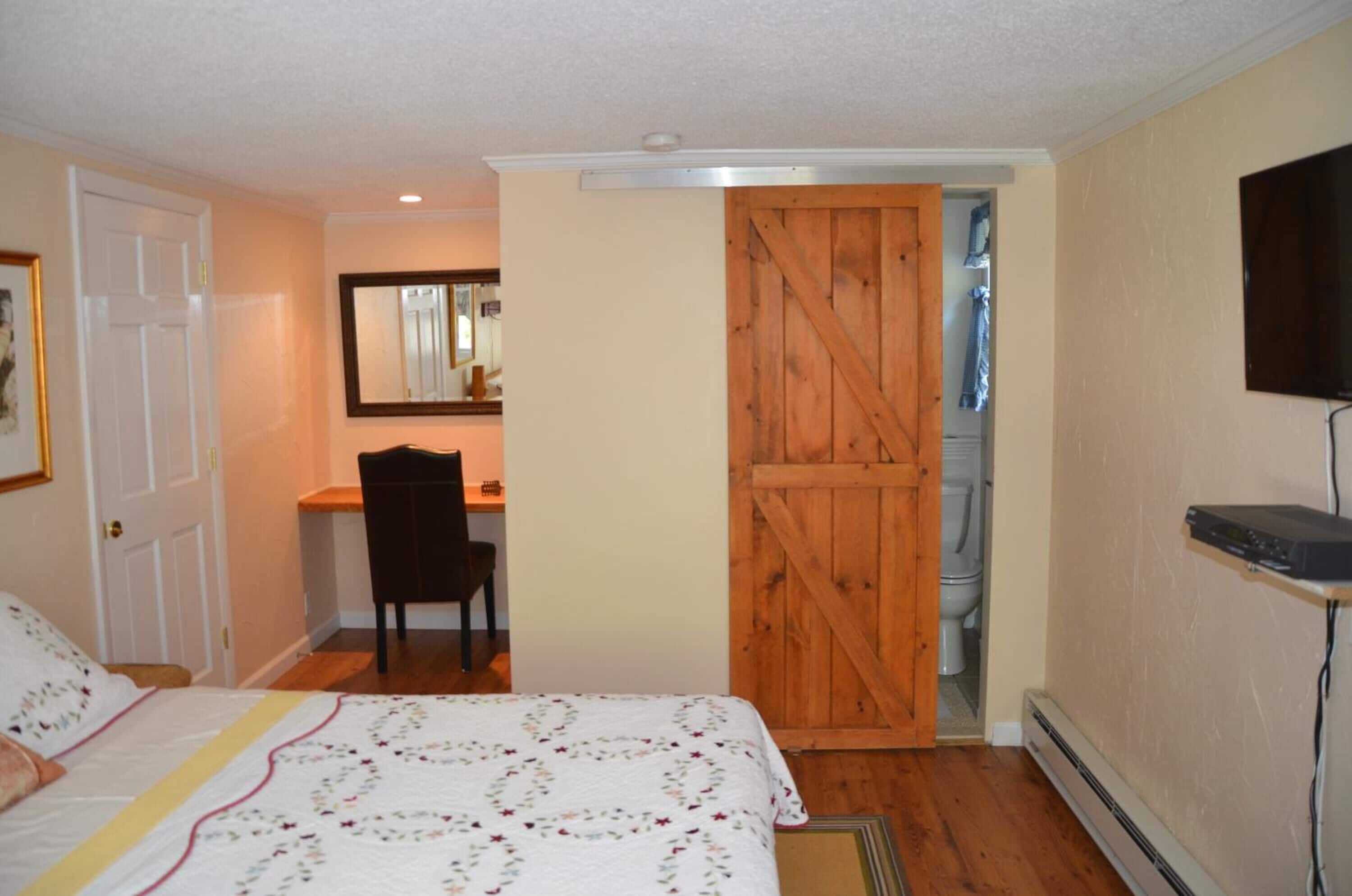 Un dormitorio con cama, escritorio, silla, puerta de madera, televisor y calentador.