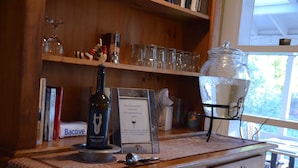 Una barra de madera con una botella de vino, copas y un cartel.