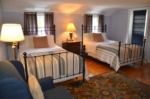 Quarto com duas camas, uma mesinha de cabeceira com abajur, tapete estampado e uma janela com cortinas.