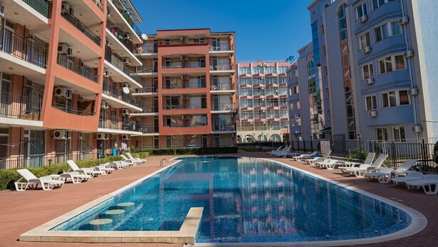 Una piscina rodeada de tumbonas y un edificio de varios pisos con balcones.