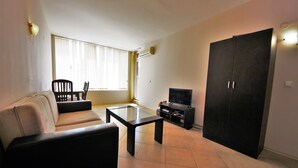 Una sala de estar con sofá, una mesa de centro de vidrio, televisión y armario.