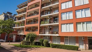Un edificio residencial de varios pisos con balcones, unidades de aire acondicionado y un camino de ladrillo que lleva a la entrada.
