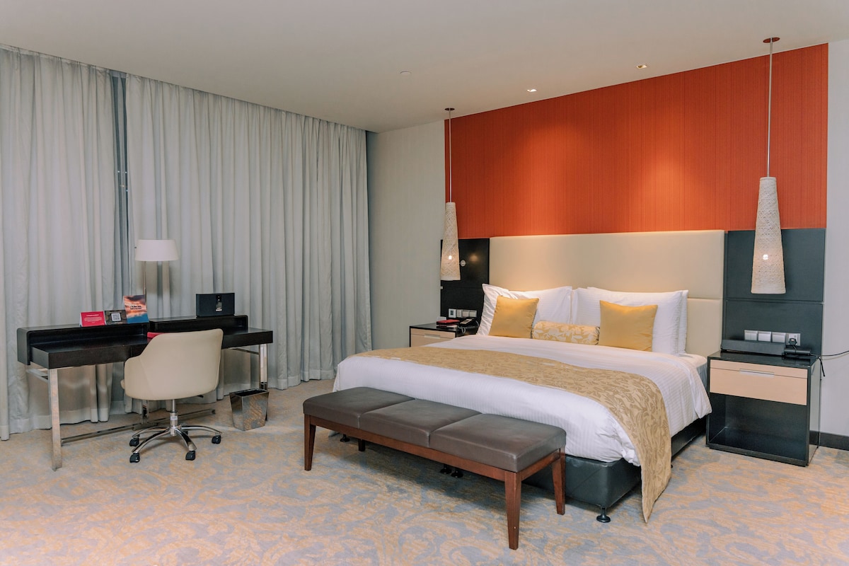 A hotel room with a bed, desk, chair, and a small bench.