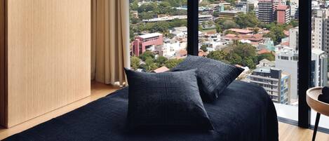A modern bedroom with a city view, a wooden wardrobe, and a small side table with towels.