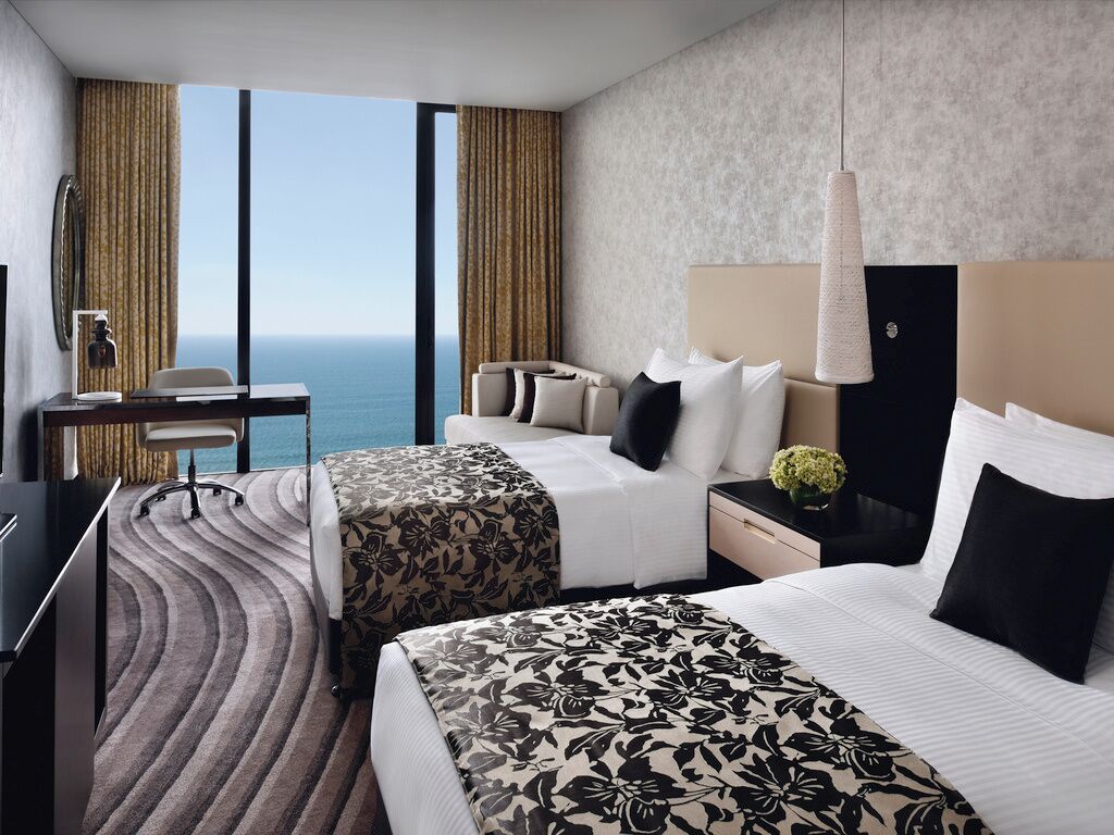 A hotel room with two beds, a desk, a chair, and a view of the ocean.