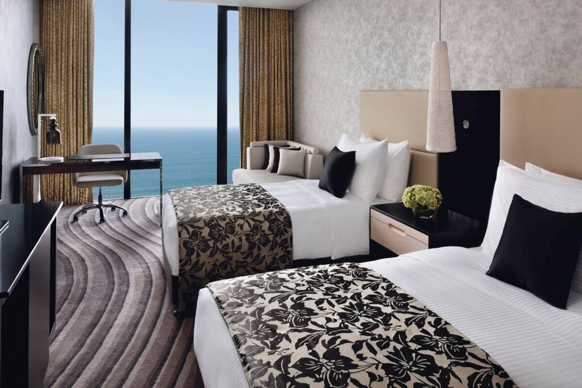 A hotel room with two beds, a desk, a chair, and a view of the ocean.