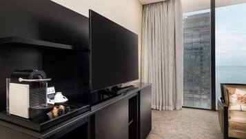 A hotel room with a flat-screen TV, a coffee machine, and a view of a building through a window.
