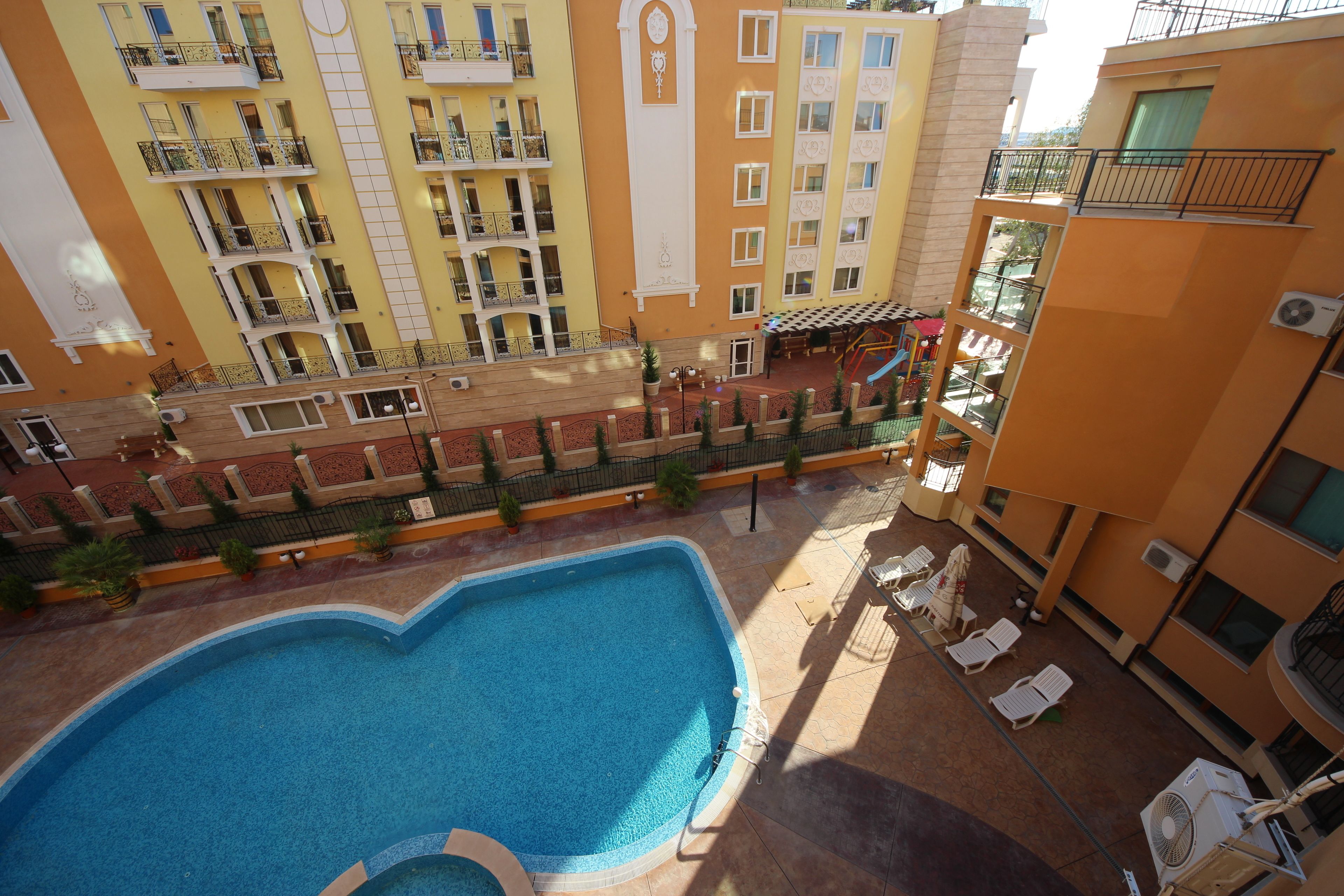 A swimming pool surrounded by a courtyard with lounge chairs and a small bridge.