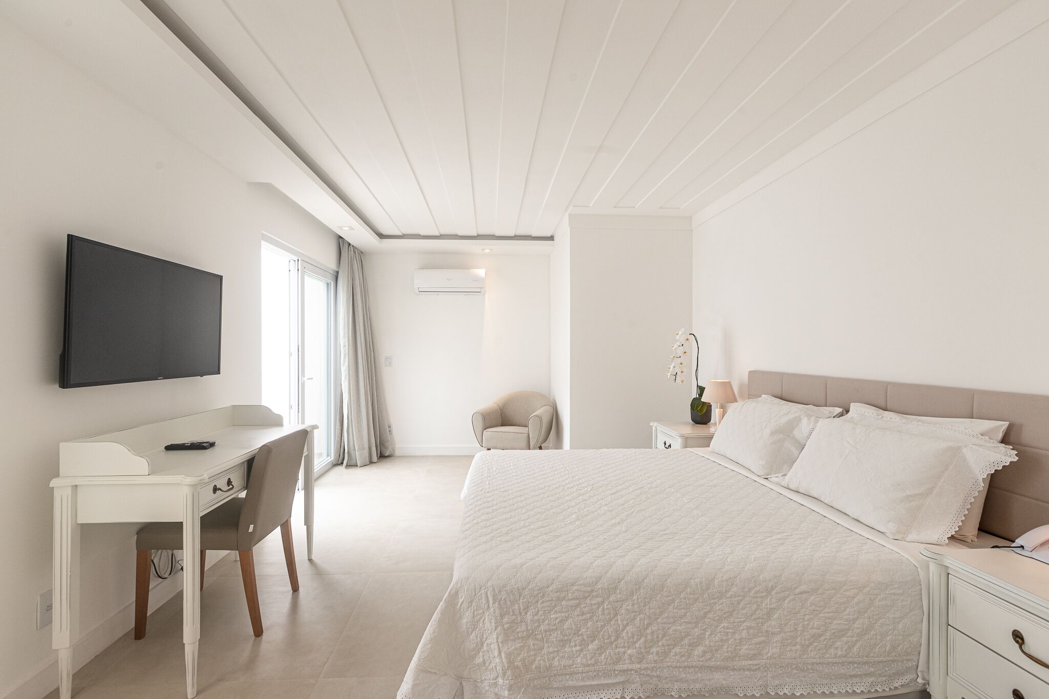 Une chambre d’hôtel avec un lit, un bureau, une chaise, une télévision et une fenêtre avec des rideaux.