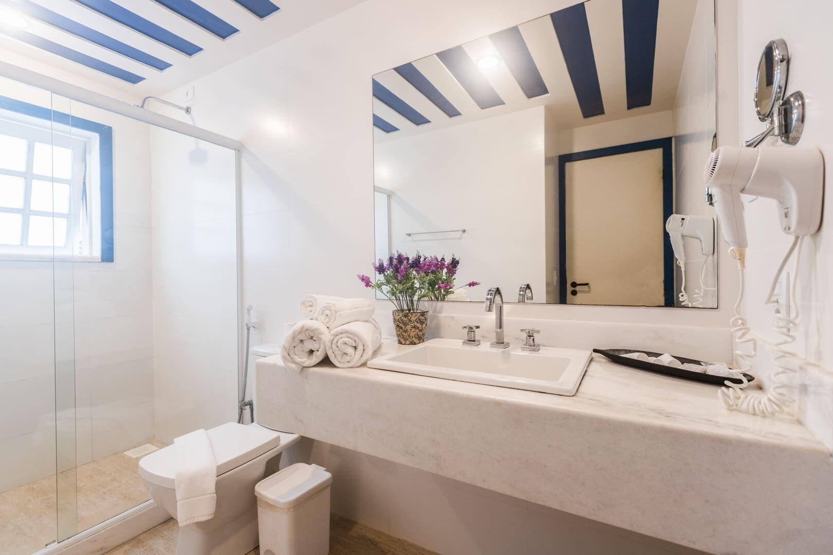 A modern bathroom with a large mirror, white sink, and a hairdryer on the counter.