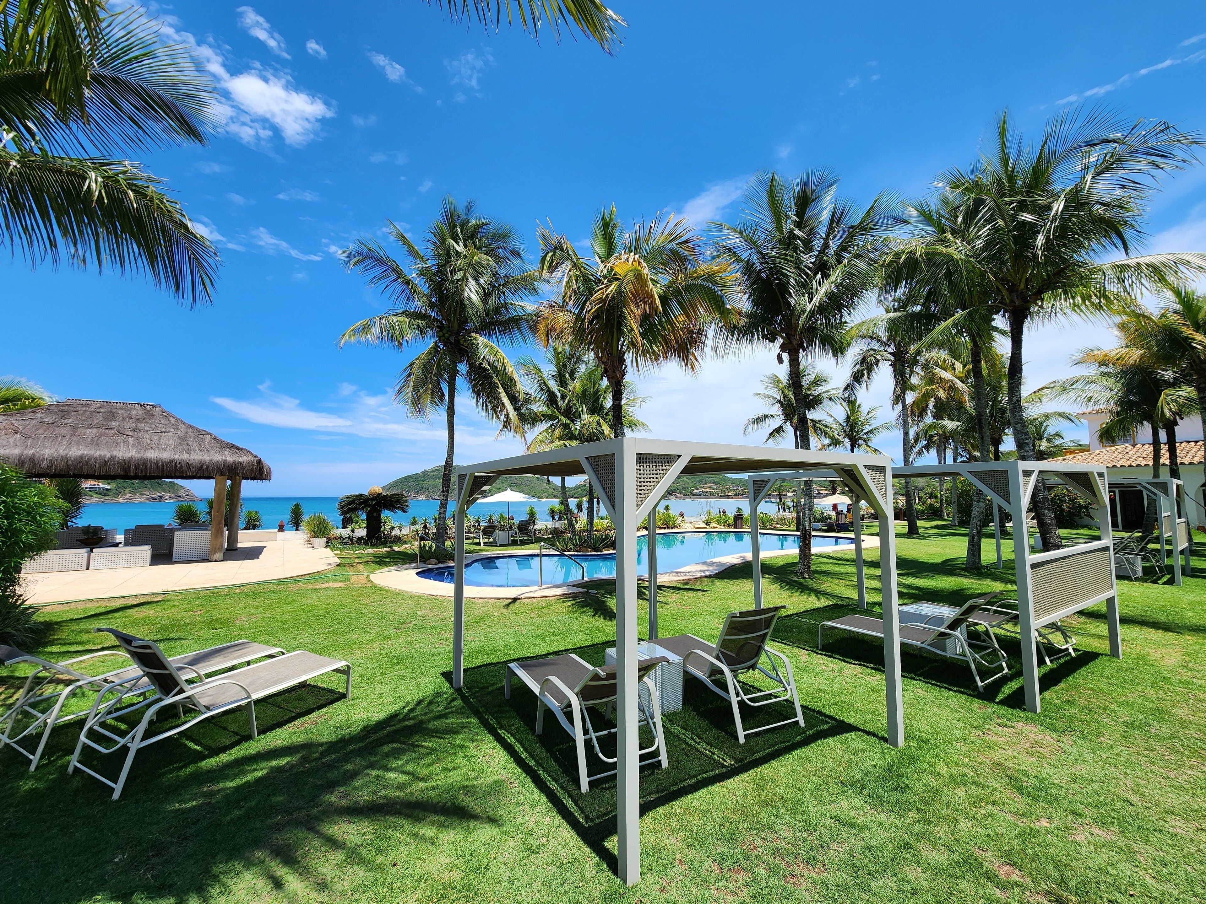 Un espace aménagé au bord de la piscine, avec des chaises longues, un coin salon abrité et une vue sur l’océan.