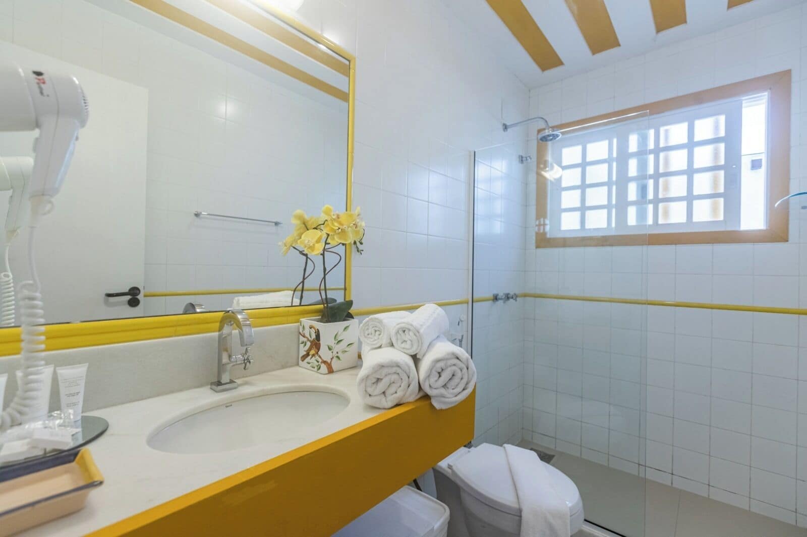 A bathroom with a white sink, yellow countertop, and a glass shower enclosure.