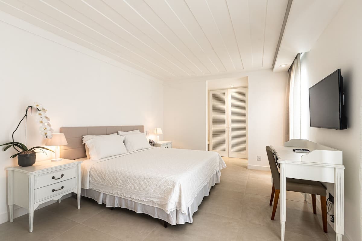 Une chambre à coucher comprenant un lit, des tables de chevet, un bureau, une chaise, un téléviseur et une plante en pot.