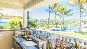 A bar area with a view of a pool and palm trees. - Villa Raphael (Búzios)