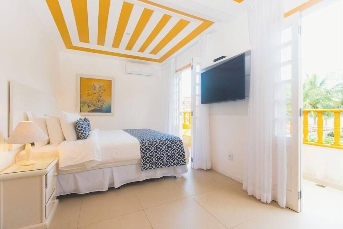 Une chambre à coucher avec un lit, une table de chevet, un téléviseur et une fenêtre avec des rideaux.