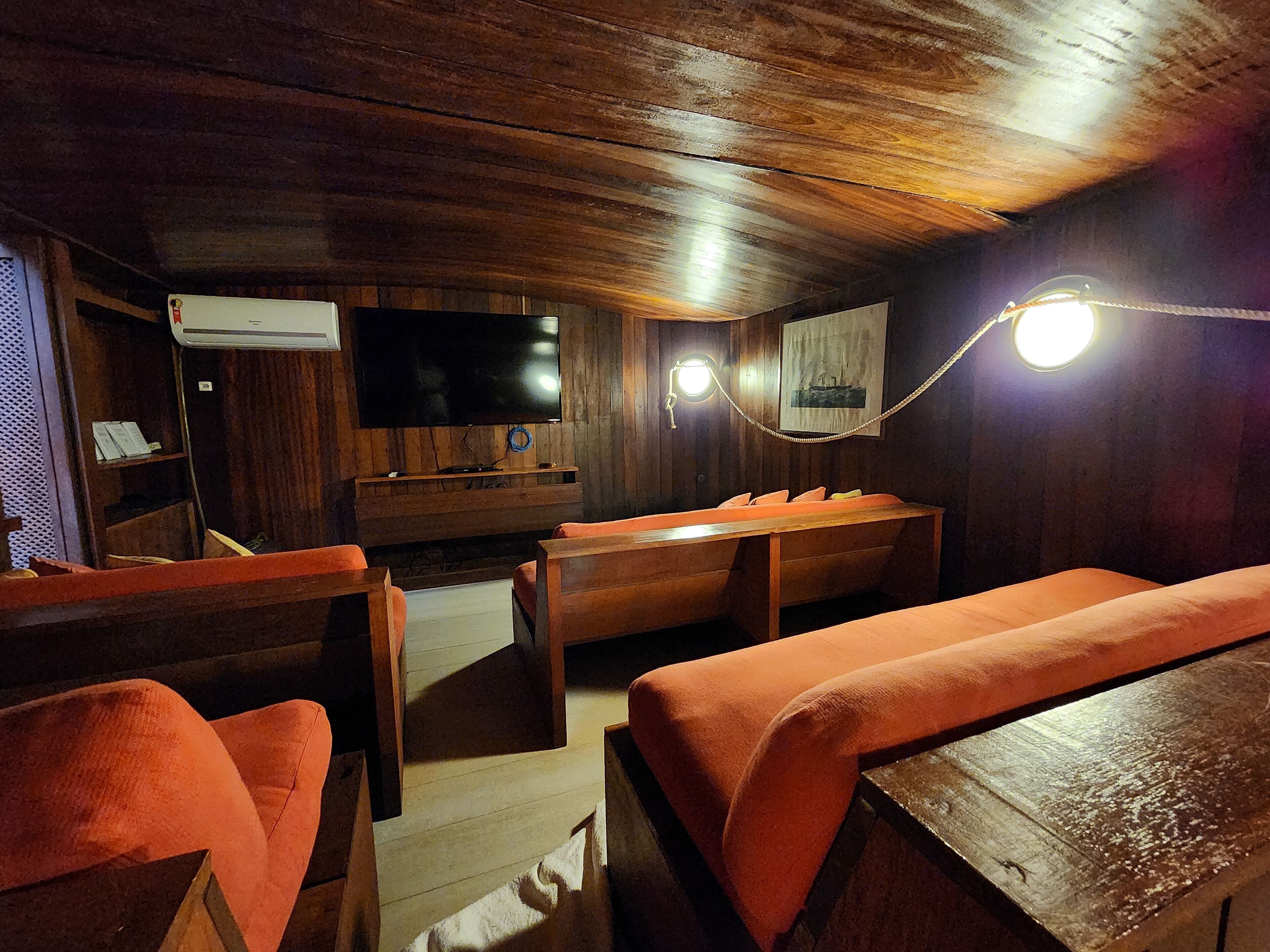 A cozy room with wooden walls and ceiling, a flat-screen TV mounted on the wall, a wooden bench, and a table.