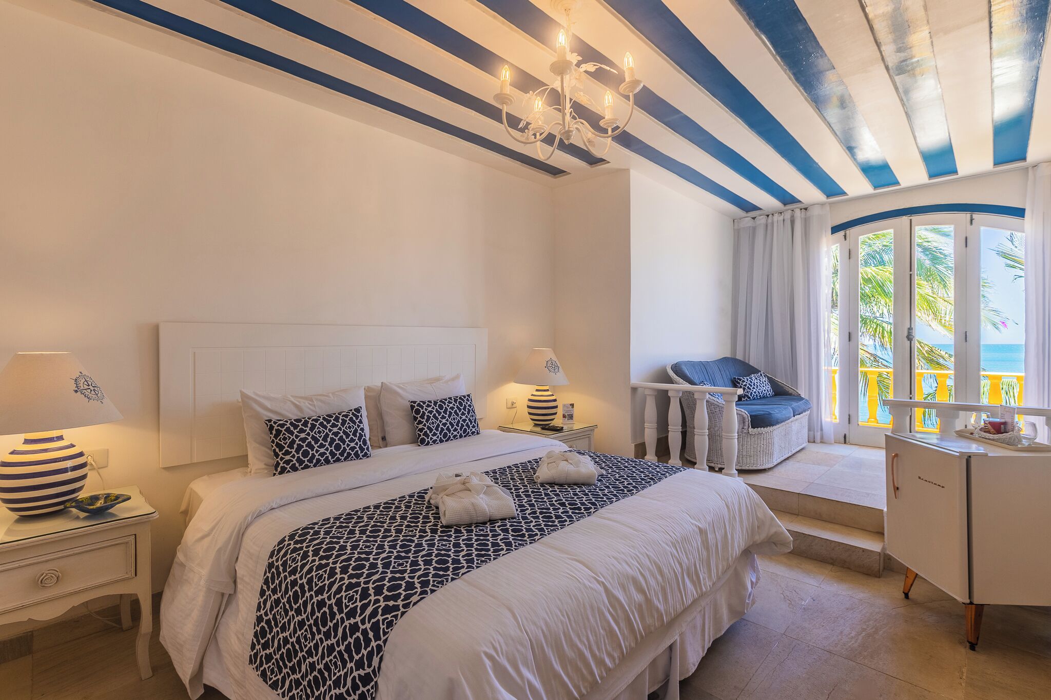 Une chambre à coucher comprenant un lit, des tables de chevet, une commode, un bureau, une chaise et une fenêtre avec des rideaux.