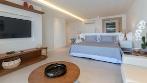 A modern bedroom with a large bed, a TV mounted on the wall, a wooden console table, and a bedside table with a lamp. - Villa Raphael (Búzios)