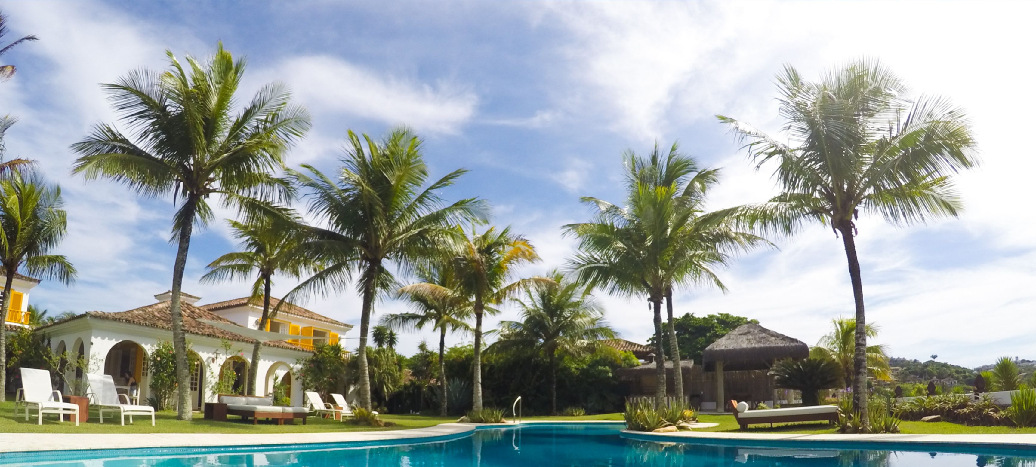 A pool area with palm trees, lounge chairs, and a building with arches.