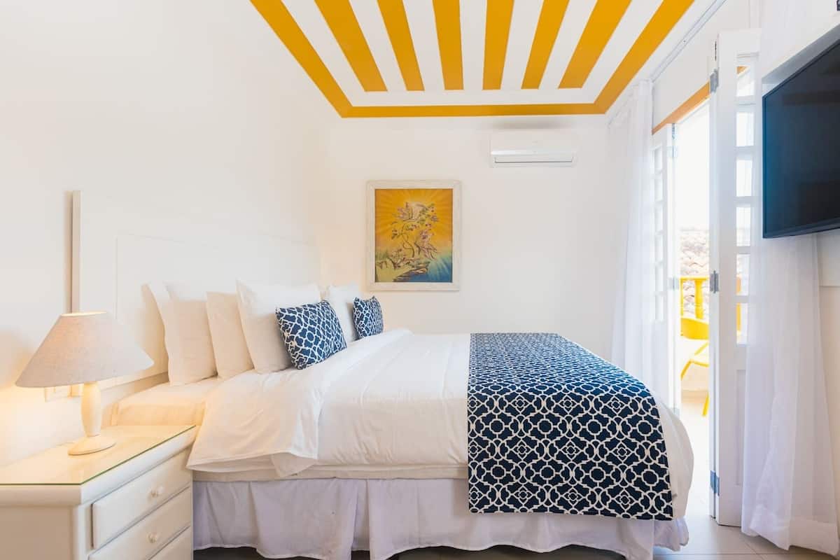 Une chambre à coucher avec un lit, une table de chevet avec une lampe, un tableau au mur et une fenêtre avec des rideaux.