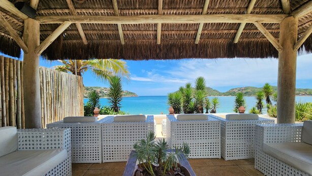 A covered outdoor seating area with a view of the sea, wooden beams, and potted plants. - Villa Raphael (Búzios)