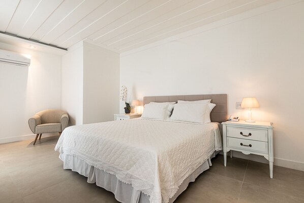 Un dormitorio con una cama grande, dos mesitas de noche con lámparas, una silla y un aire acondicionado.