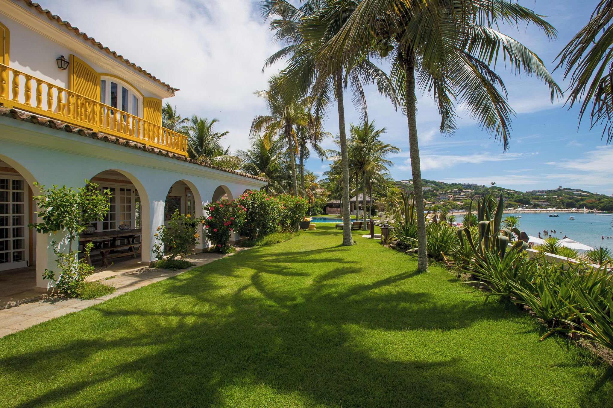 Un jardín cuidado con piscina, palmeras y vista al mar.