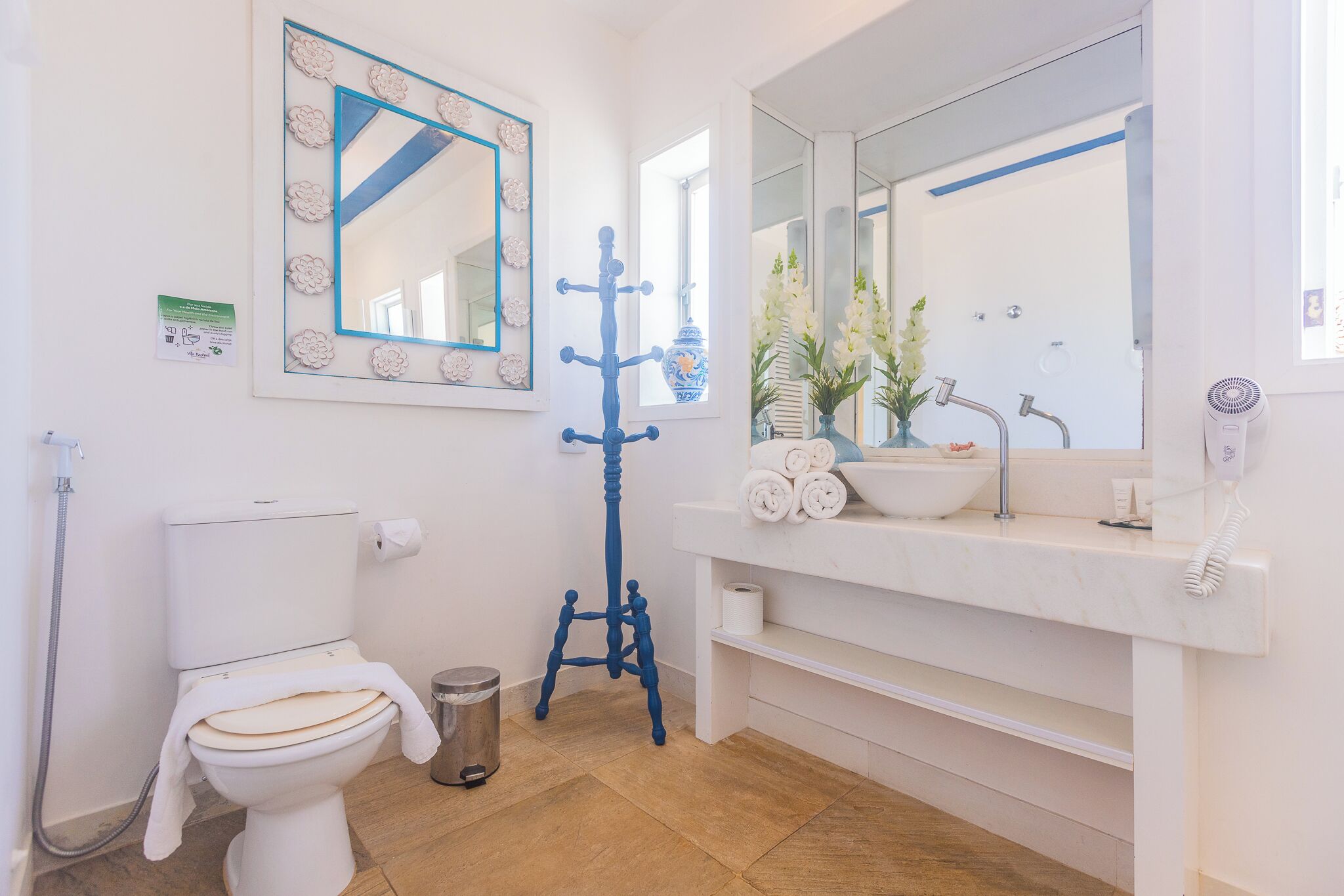 Une salle de bain avec des toilettes, un lavabo avec un miroir, un porte-manteau bleu et une plante en pot.