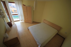 A bedroom with a bed, a wardrobe, a desk, and a window with curtains.