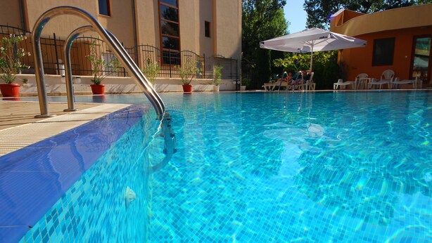 A clear swimming pool with a metal ladder, potted plants, and lounge chairs. - Menada Amadeusz 1 Apartments (Sunny Beach)