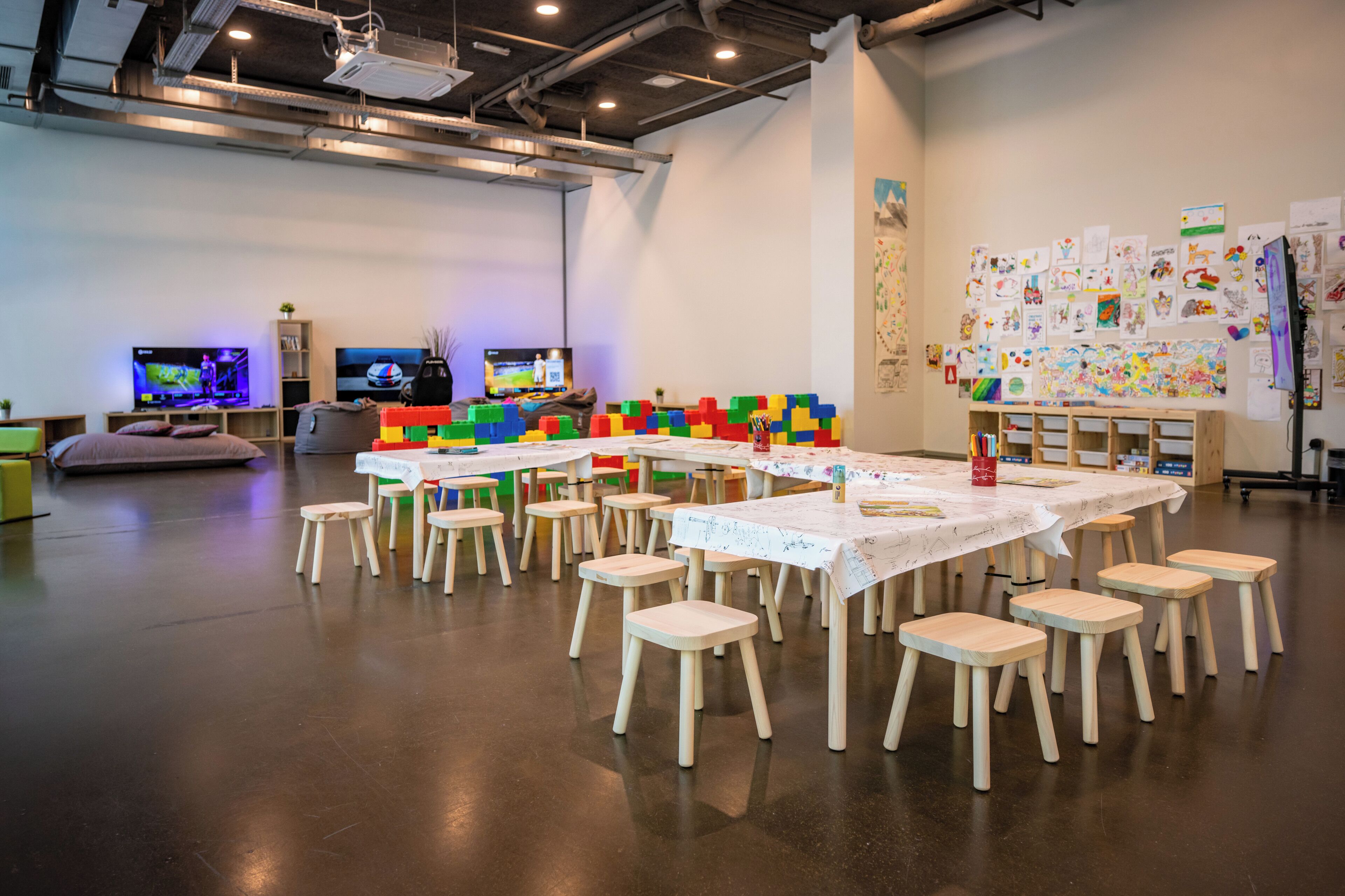 A spacious room with multiple tables and chairs, a television, and children's artwork on the walls.