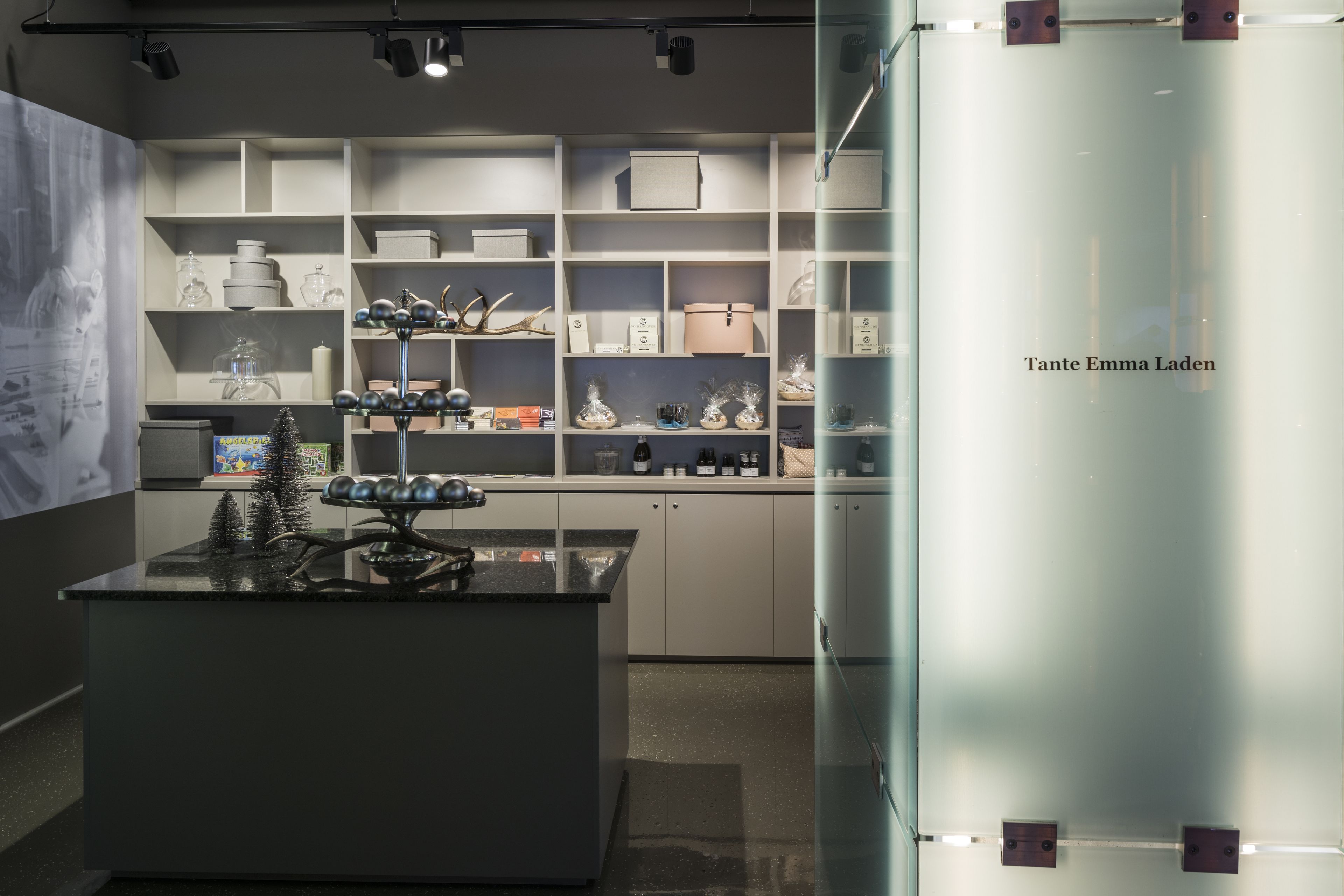 A modern interior with glass display cases and shelves, a central black table with decorative items, and a wall with a framed picture.