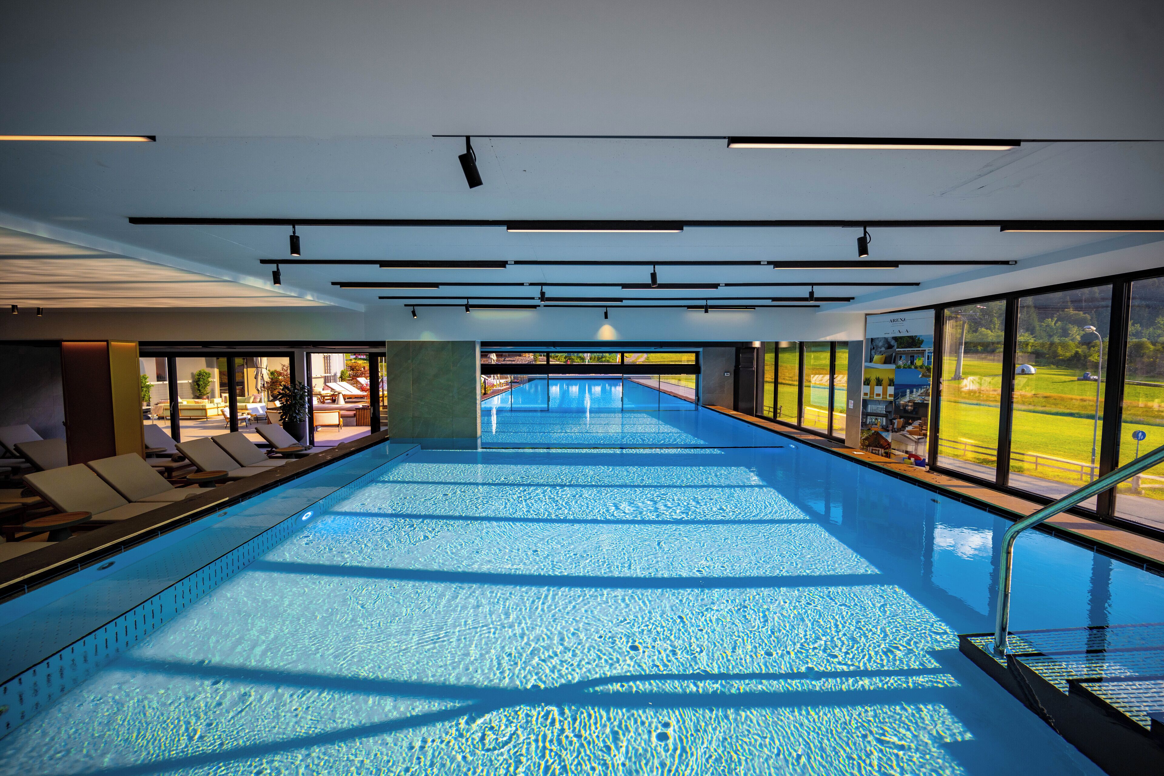 Una grande piscina coperta con acqua cristallina e illuminata lateralmente, con vista su un campo da golf attraverso ampie finestre.