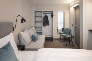 Una habitación de hotel con cama, sofá, escritorio con una computadora portátil, silla, armario y espejo.