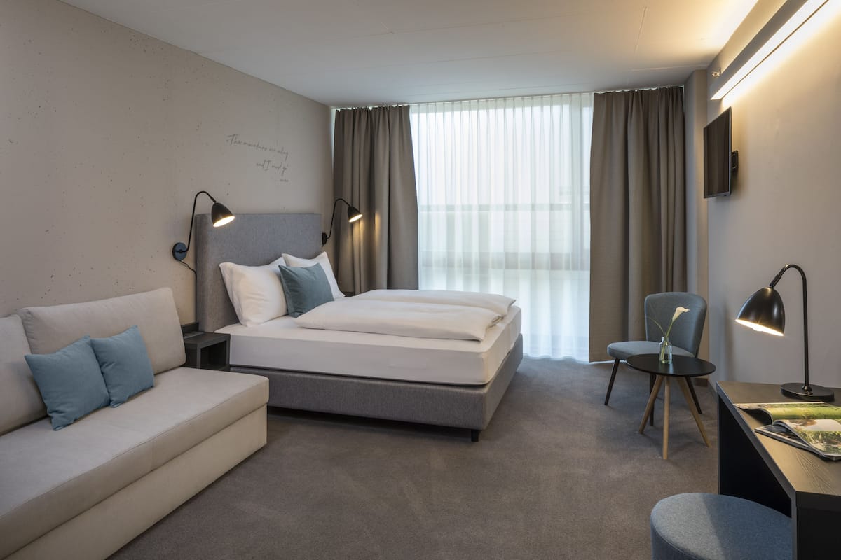Una habitación de hotel moderna con cama, sofá, escritorio y silla.