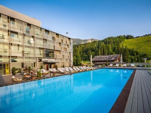 Un hôtel doté d’une piscine, de chaises longues et offrant une vue sur un paysage montagneux.