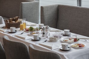 Una mesa de desayuno dispuesta con varios platos, incluyendo huevos, tostadas y fruta, junto con tazas y vasos.