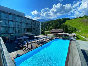 Un hotel moderno con piscina, sillones de descanso y vistas a las montañas.